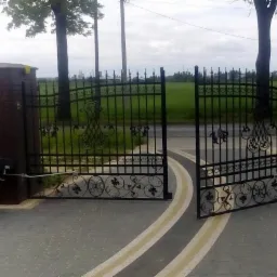 Montaż automatyki do ozdobnej, kutej bramy wjazdowej z ceglanymi słupkami. Widoczny monter w trakcie podłączania sterownika.