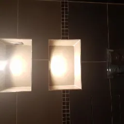 Nowoczesna łazienka z czarnymi płytkami, dwoma wnękami z oświetleniem punktowym i chromowanym przyciskiem spłuczki