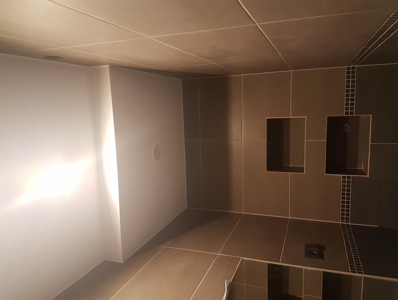 Nowoczesna łazienka z ciemnymi płytkami i wnękami w ścianie, minimalistyczny design z ukrytym odpływem liniowym.