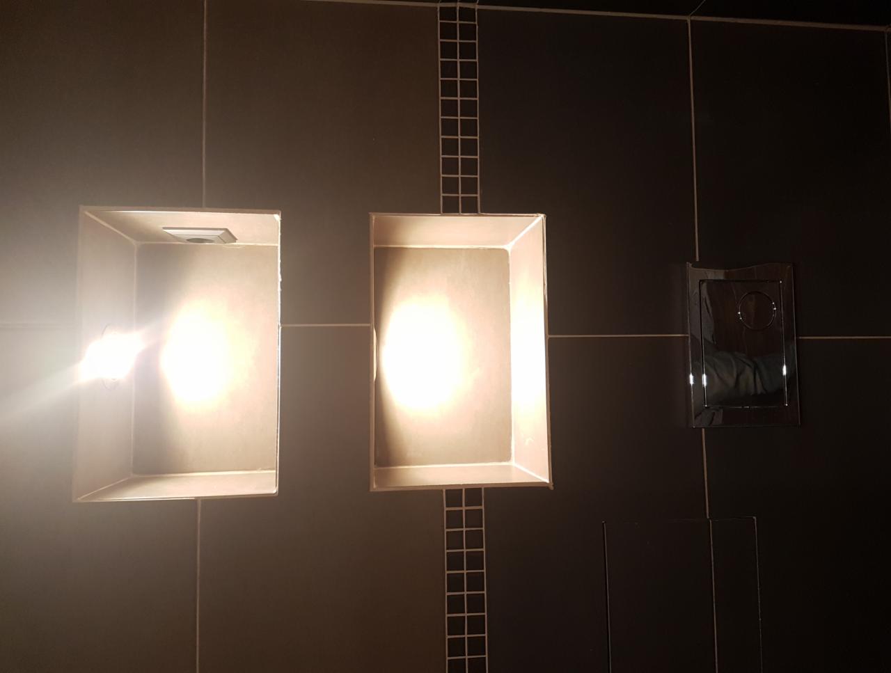 Nowoczesna łazienka z czarnymi płytkami, dwoma wnękami z oświetleniem punktowym i chromowanym przyciskiem spłuczki