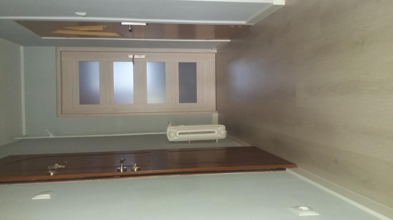 Widok wnętrza pokoju z zamontowanymi drzwiami przesuwnymi z szybami, grzejnikiem elektrycznym na ścianie i fragmentem podwieszanego sufitu.