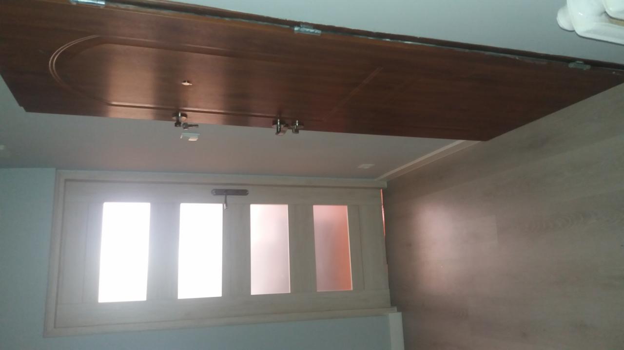 Drewniane drzwi przesuwne zamontowane pod sufitem, widoczne zawiasy i prowadnice, jasna podłoga i ściany.