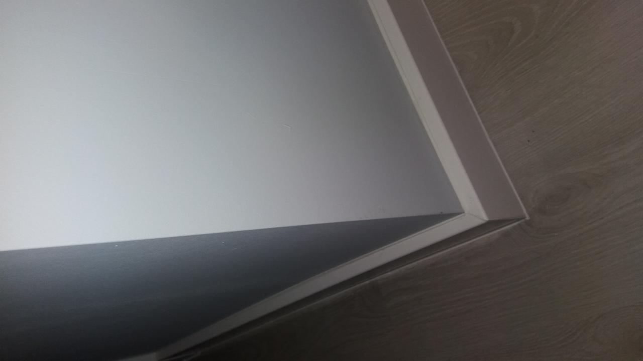 Fragment pomalowanego na biało sufitu z widoczną listwą przypodłogową i fragmentem podłogi imitującej drewno.