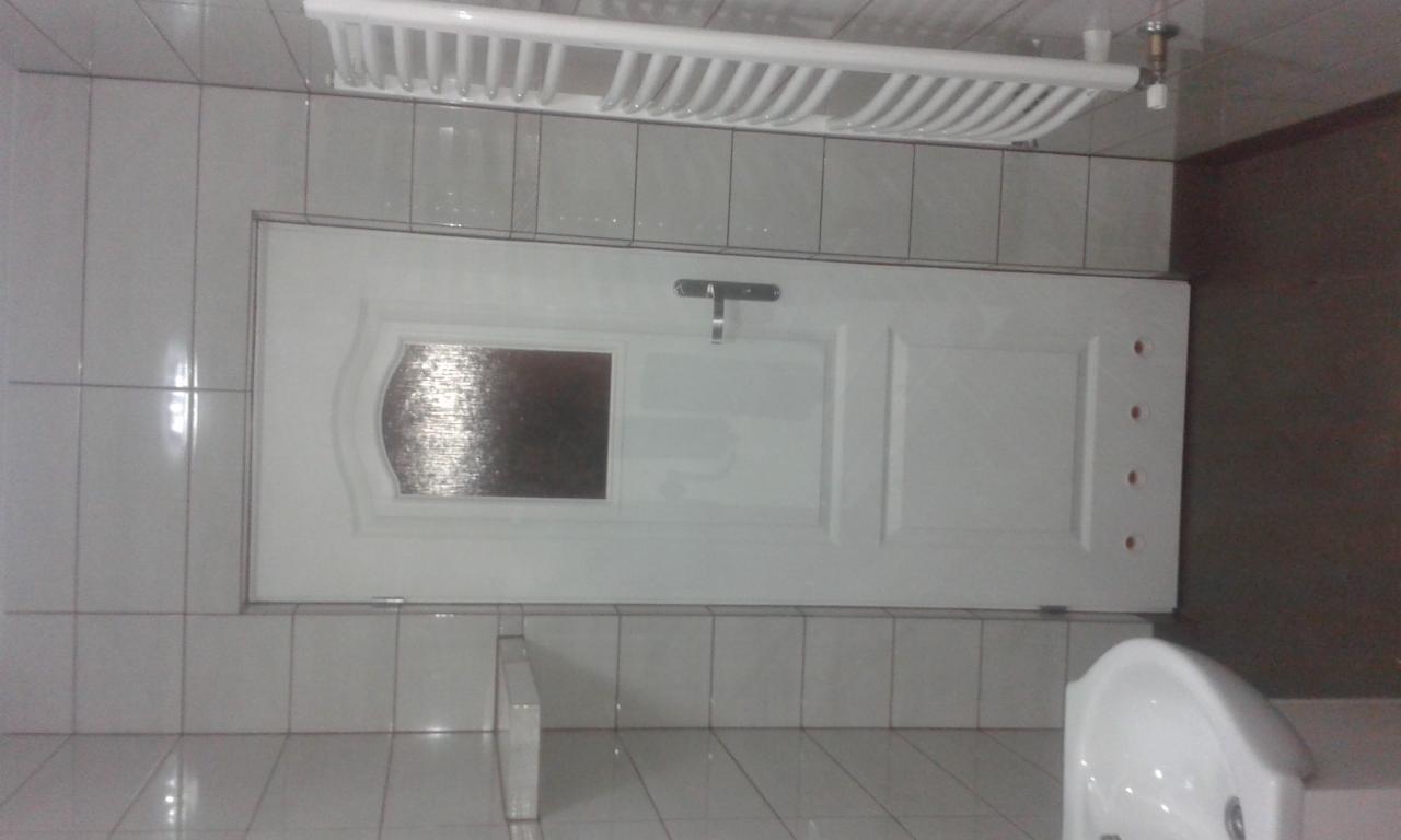 Wykończona łazienka z białymi płytkami, białą umywalką i białą, częściowo przeszkloną, zamontowaną futryną drzwiową oraz grzejnikiem drabinkowym na ścianie.