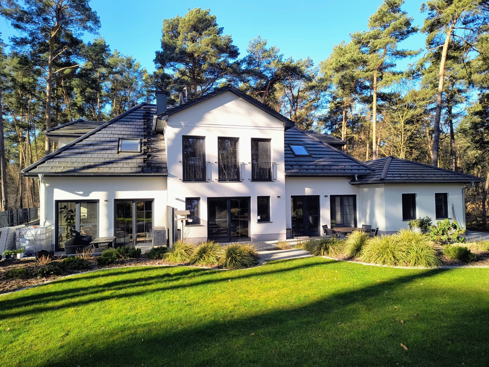 Elewacja nowoczesnego, dwupiętrowego domu w Szczecinie z czarnymi oknami PCV, ciemną dachówką i zadbanym trawnikiem w słoneczny dzień.