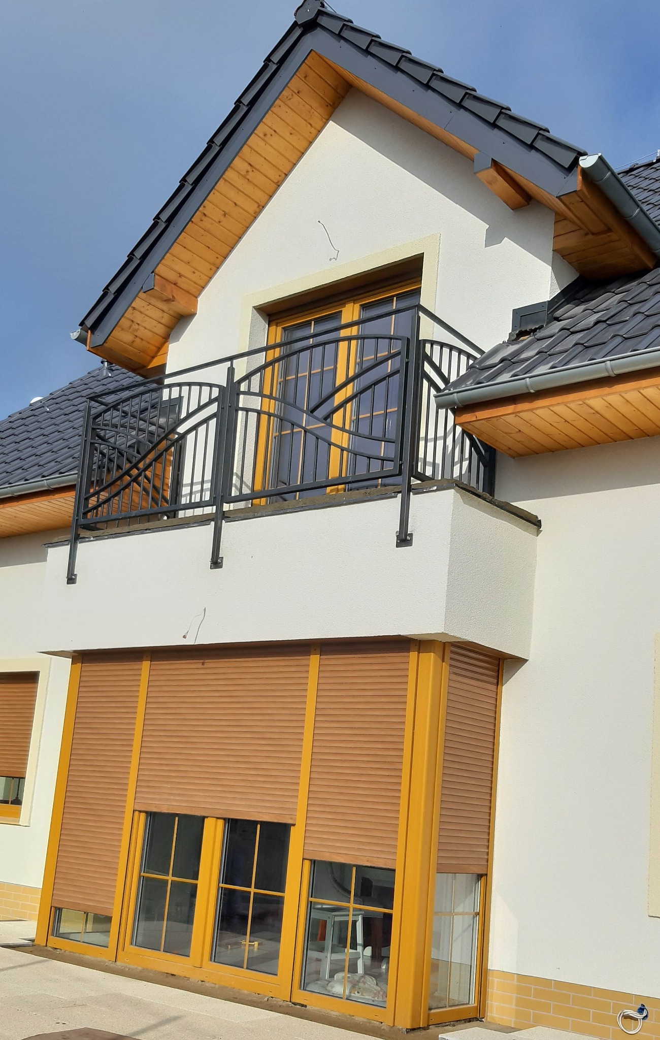 Elewacja domu w Szczecinie z oknami z brązowymi roletami zewnętrznymi, balkon z czarną metalową balustradą i stolarką okienną w kolorze drewna.