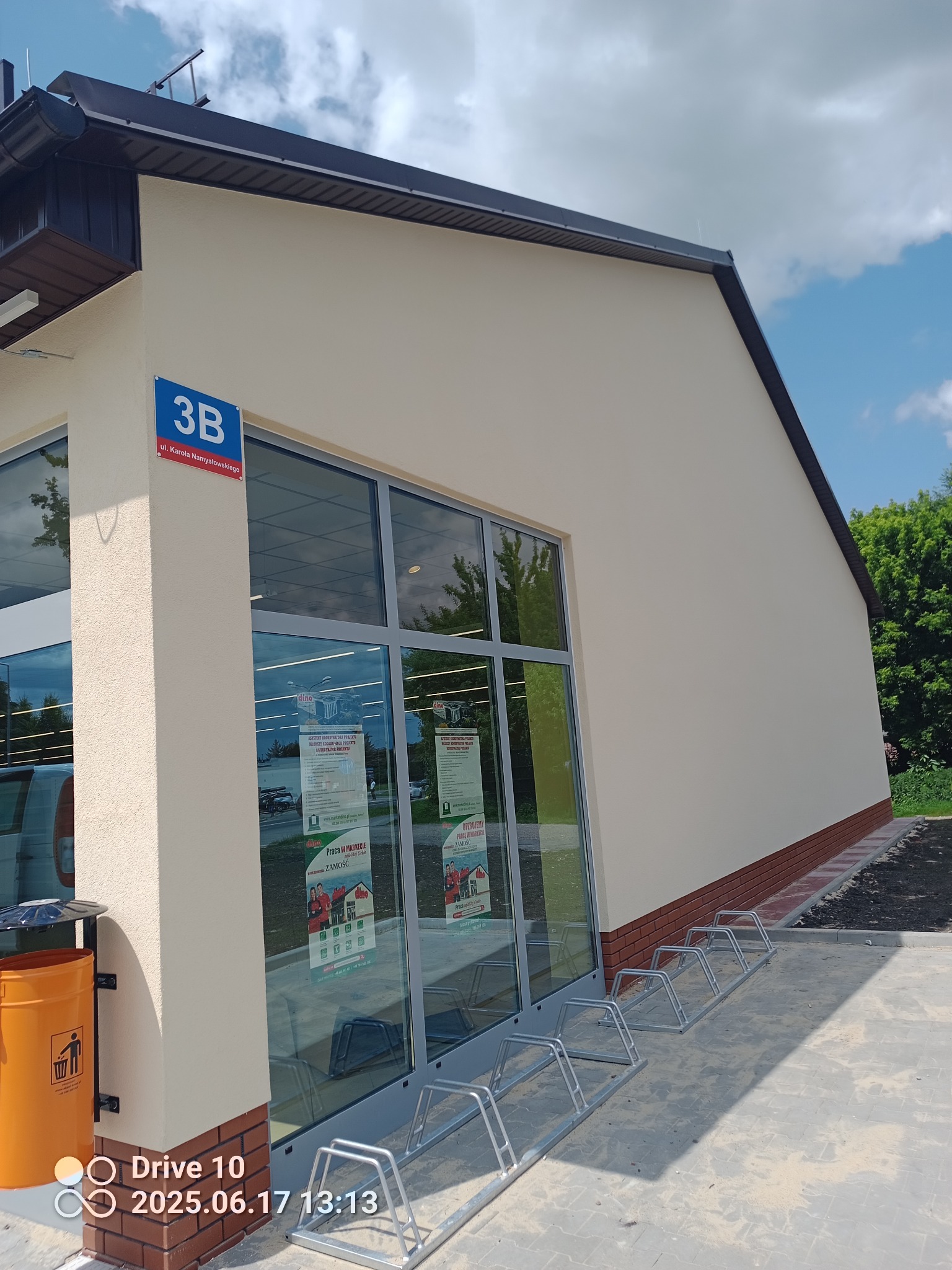 Jasna elewacja budynku z numerem 3B przy ulicy Karola Namysłowskiego, widoczna z perspektywy narożnej, w słoneczny dzień. Na dole widoczne ceglane wykończenia.