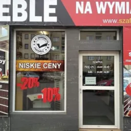 Fasada sklepu z wyposażeniem wnętrz w Piasecznie, z widocznymi plakatami informującymi o ofercie i promocjach na meble oraz godzinach otwarcia.