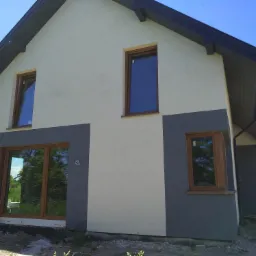 Dwukolorowa elewacja domu jednorodzinnego z drewnianą stolarką okienną, świeżo po ukończeniu prac, widok z zewnątrz na tle błękitnego nieba.