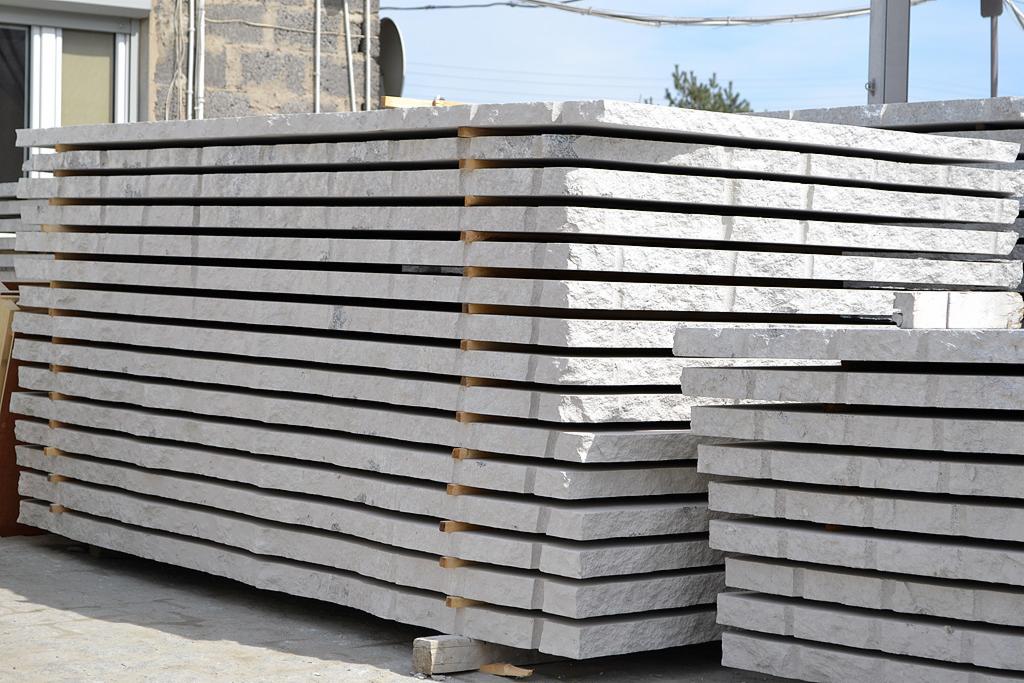 Stos szarych płyt kamiennych ułożonych na drewnianych legarach, widoczne nierówności krawędzi i tekstura kamienia.