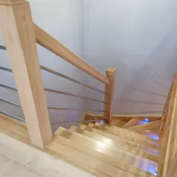 Drewniane schody z metalowymi poręczami, podświetlane niebieskim światłem, widok z góry.