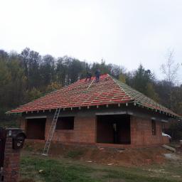 USŁUGI OGÓLNOBUDOWLANE TERLECKI - Budowa domu jednorodzinnego w stanie surowym otwartym, z widoczną konstrukcją dachu pokrytą czerwoną membraną i łatami, na tle jesiennego lasu.