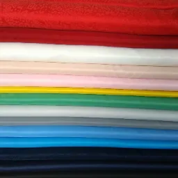 Stos kolorowych tkanin, od czerwonej z delikatnym wzorem po czarną, ułożonych jedna na drugiej, ukazujących różnorodność materiałów.