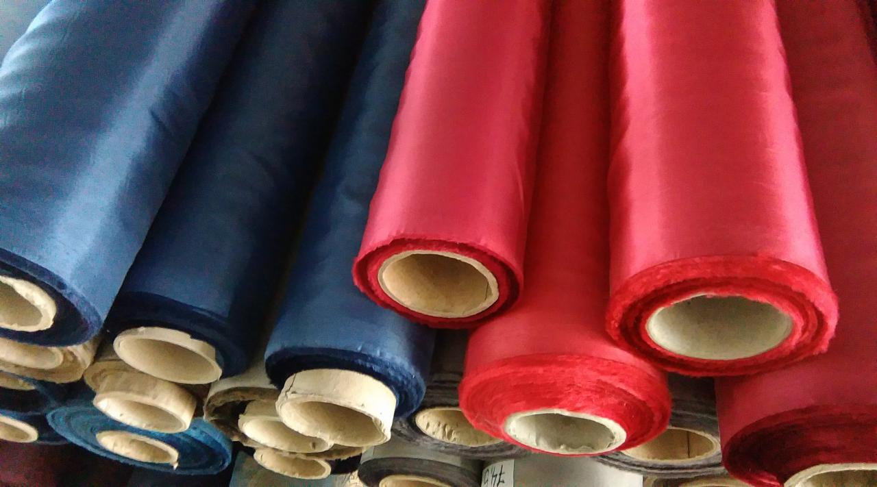 Rzędy nawiniętych rolek tkanin w odcieniach niebieskiego i różowego, widoczne tekturowe rdzenie, ujęcie z dołu.