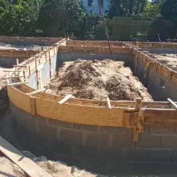 Fundament domu z bloczków betonowych z drewnianym szalunkiem, częściowo wypełniony ziemią, widok z góry.
