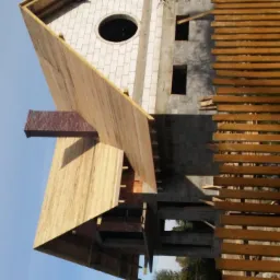 Wznoszony budynek z białego bloczka z okrągłym oknem, widoczne drewniane szalunki i rusztowanie, komin z cegły. Ujęcie z dołu pod kątem.