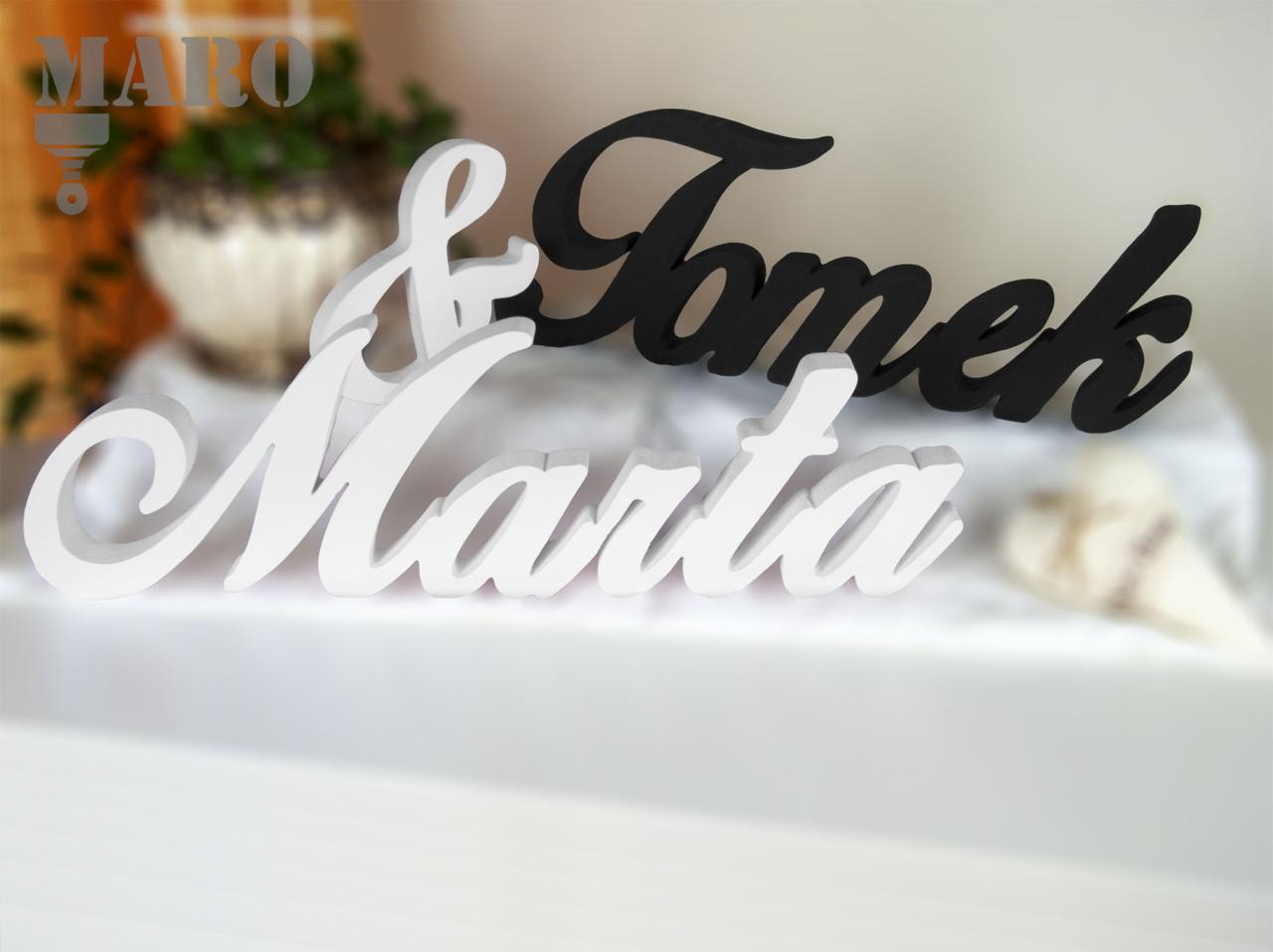 Dekoracyjne, przestrzenne napisy imion Marta i Tomek w kolorze białym i czarnym, połączone znakiem '&', ustawione na białym tle z rozmyciem, sugerujące prezent ślubny lub walentynkowy.
