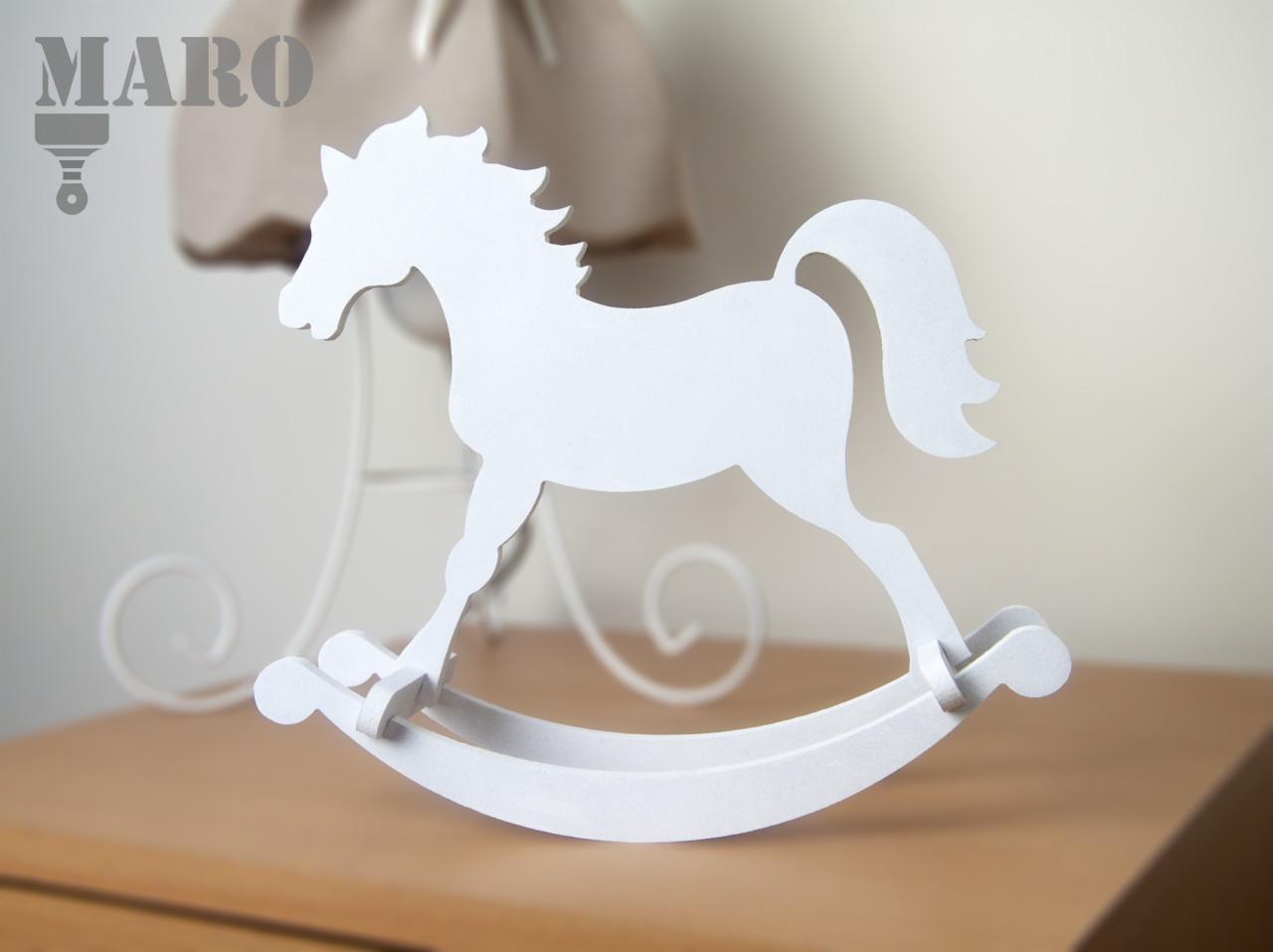 Biały, drewniany konik na biegunach, dekoracja stołu w Wtelnie, z widocznym logo MARO w tle, obok lampki z beżowym abażurem.