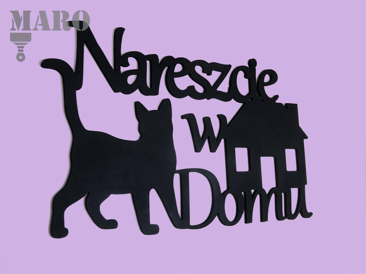 Czarna, wycinana laserowo dekoracja ścienna z napisem 'Nareszcie w Domu', sylwetką kota i domku na fioletowym tle.