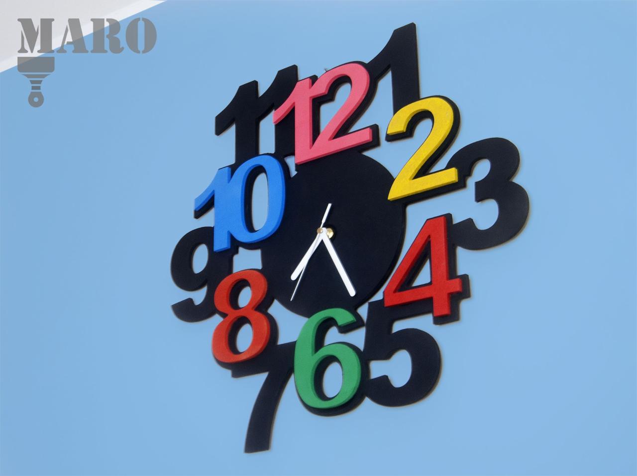 Kreatywny zegar ścienny z czarną tarczą i kolorowymi, trójwymiarowymi cyframi na niebieskim tle, wskazówki ustawione na godzinę 11:59.