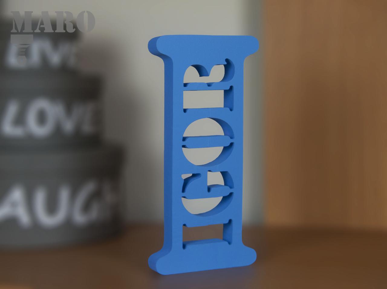 Niebieska, pionowa dekoracja z wyciętym napisem 'Igor', na rozmytym tle z napisem 'MARO LIVE LOVE LAUGH'.