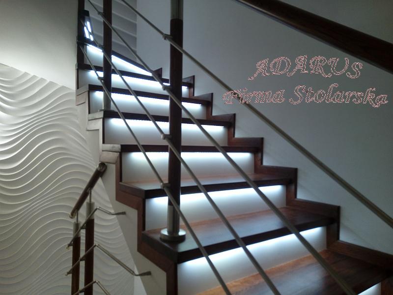 Nowoczesne schody z ciemnego drewna z podświetleniem LED pod każdym stopniem i metalową balustradą, obok ściana z dekoracyjnym wzorem fal.