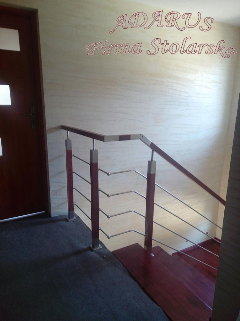Klatka schodowa z ciemnego drewna i metalowymi relingami, widoczne logo firmy stolarskiej na ścianie