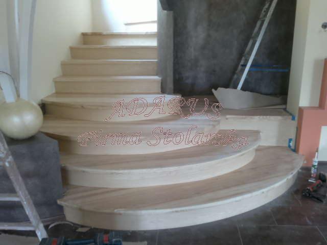 Montaż drewnianych schodów z zaokrąglonymi stopniami, widoczne narzędzia i drabina, etap wykończeniowy.