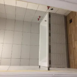 Białe i szare płytki ułożone w łazience, z widocznymi krzyżykami dystansowymi, drewnopodobna okładzina ściany po prawej, fragment wanny.