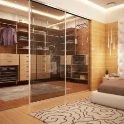Przestronna garderoba z przesuwnymi szklanymi drzwiami, widoczna z sypialni z tapicerowanym zagłówkiem i wiszącymi lampami, oświetlenie punktowe w suficie.