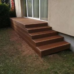 Brązowy taras kompozytowy z czterema stopniami prowadzący do przeszklonych drzwi balkonowych, widok z poziomu trawnika.