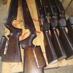 MODEL-JURA - Brązowe, lakierowane elementy drewniane, przypominające kolby karabinów, ułożone na stole z widocznymi śladami farby.