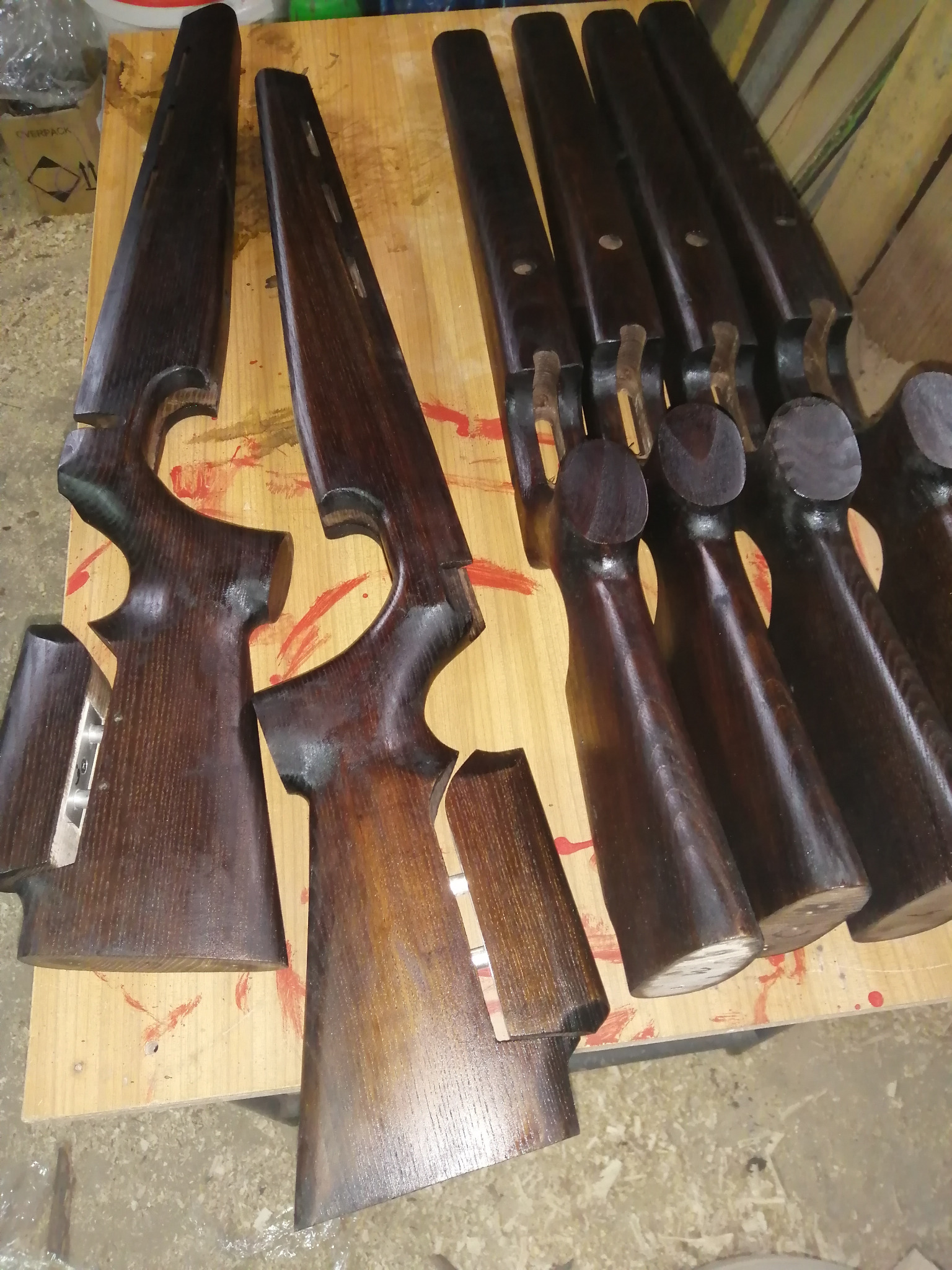 Brązowe, lakierowane elementy drewniane, przypominające kolby karabinów, ułożone na stole z widocznymi śladami farby.