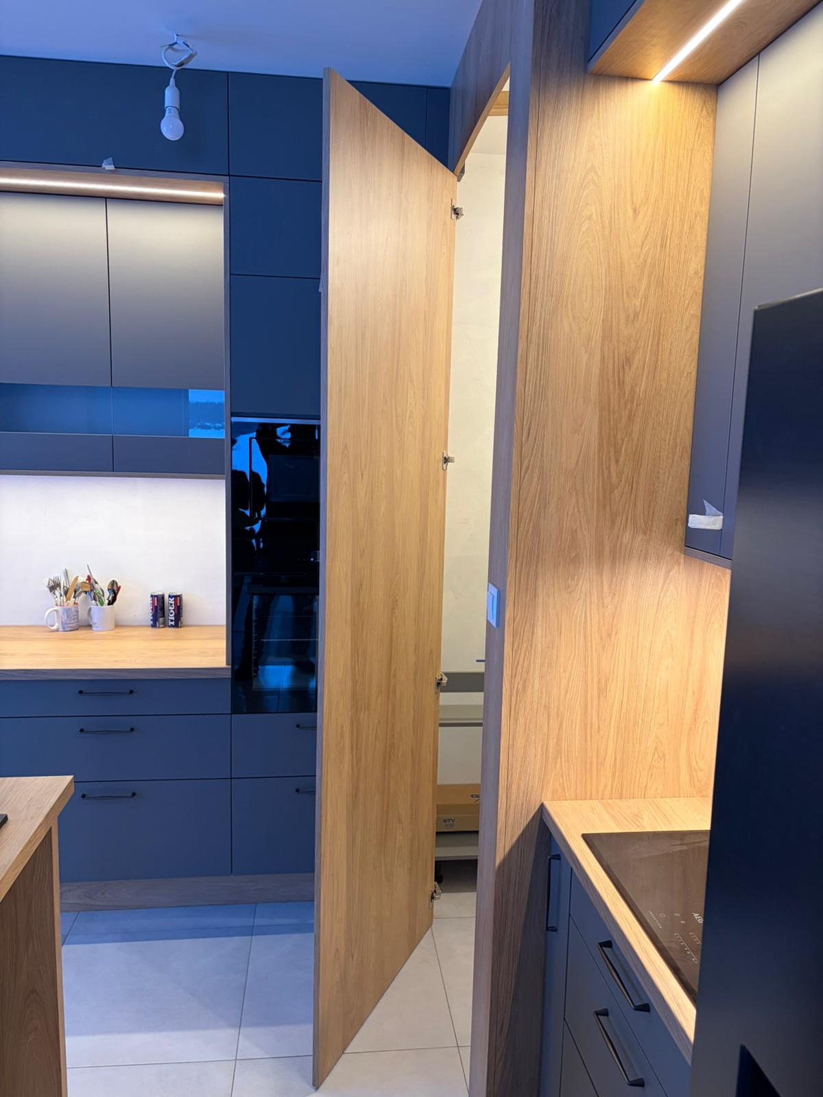 Niebieska kuchnia z drewnianymi akcentami: otwarta szafka z systemem cargo, oświetlenie LED, minimalistyczny design. Nowoczesne rozwiązanie do przechowywania.