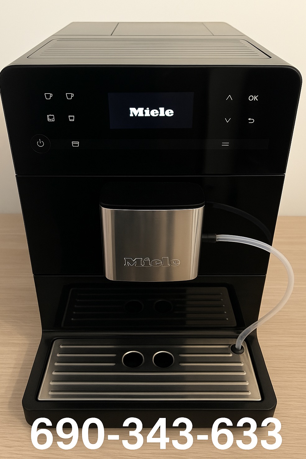 Czarny ekspres do kawy Miele z podłączonym pojemnikiem na mleko i wyświetlaczem. Widoczny numer telefonu na dole zdjęcia.