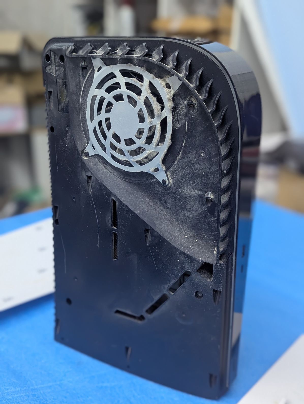 Zanieczyszczony wentylator konsoli PlayStation 5 z widocznymi żeberkami chłodzącymi i otworami wentylacyjnymi. Widok z tyłu, ukazujący detale konstrukcyjne.