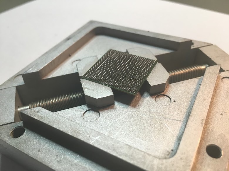 Układ BGA w metalowym imadle warsztatowym, przygotowany do lutowania. Widoczne kulki lutownicze na powierzchni układu. Sprzęt serwisowy w warsztacie elektroniki.