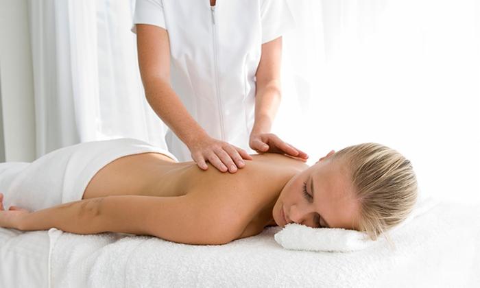 Kobieta leży na brzuchu podczas masażu pleców, wykonywanego przez osobę w białym uniformie, w jasnym pomieszczeniu z białymi zasłonami.