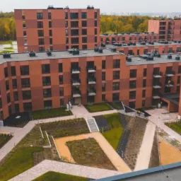 Widok z góry na osiedle budynków wielorodzinnych z cegły, z wewnętrznym dziedzińcem z zielenią i ścieżkami.