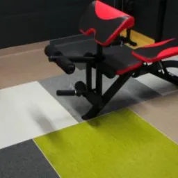 Patchworkowa podłoga z kwadratowych wykładzin dywanowych w siłowni domowej, z czarną ścianą i sprzętem do ćwiczeń.