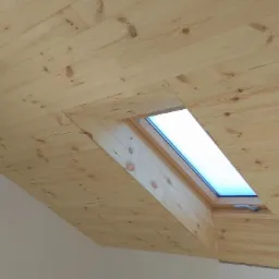 Drewniana boazeria na skośnym suficie poddasza z oknem dachowym, widoczne sęki i naturalny odcień drewna.