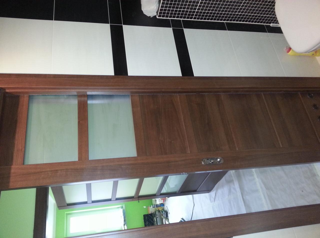 Brązowe, przeszklone drzwi przesuwne w łazience z czarno-białymi płytkami na ścianach, widoczne fragmenty zielonej ściany w kolejnym pomieszczeniu.