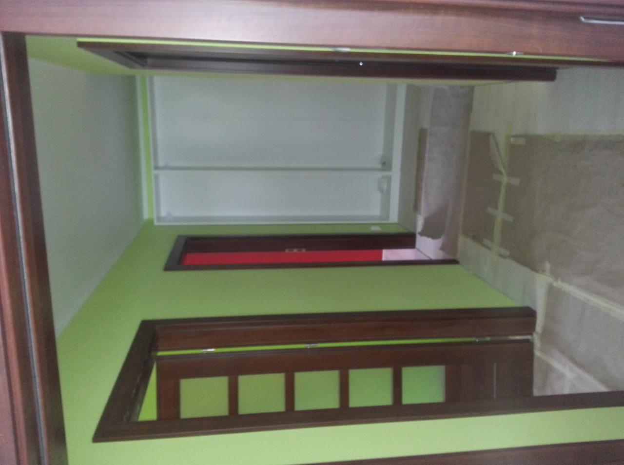 Świeżo pomalowane na zielono ściany w Starogardzie Gdańskim, z widocznymi brązowymi obramowaniami drzwi i okien, częściowo zabezpieczone folią malarską.