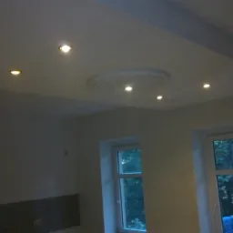 Wykończony sufit podwieszany z płyt kartonowo-gipsowych z okrągłą dekoracją i punktowym oświetleniem, widok na dwa okna.