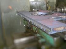 Płyta metalowa z wyciętymi otworami, mocowana do frezarki za pomocą śrub, widoczne ślady obróbki.