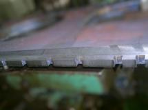 Metalowy detal z wyfrezowanymi rowkami, widoczne ślady obróbki skrawaniem, nieostre tło.