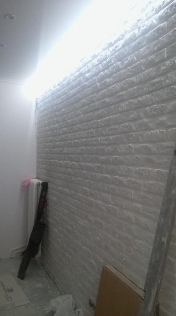 Ściana wykończona panelami imitującymi białą cegłę, widoczny grzejnik, narzędzie Bosch i drabina.