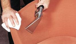 Czyszczenie tapicerki fotela pomarańczową dyszą odkurzacza ekstrakcyjnego, z widoczną białą ściereczką w dłoni osoby czyszczącej.