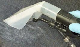 Dysza odkurzacza ekstrakcyjnego w trakcie czyszczenia ciemnej, teksturowanej tkaniny, widoczne dłonie w niebieskich rękawicach.