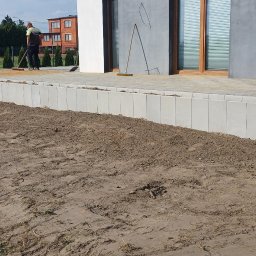 P.H.U. Węglewscy - Ukończony taras z kostki brukowej z betonowym obrzeżem, widoczny pracownik zamiatający powierzchnię, w tle dom z szarymi ścianami i brązowymi oknami.